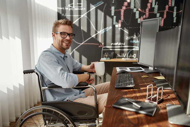 man at work in wheel chair drinking coffee in front of computer